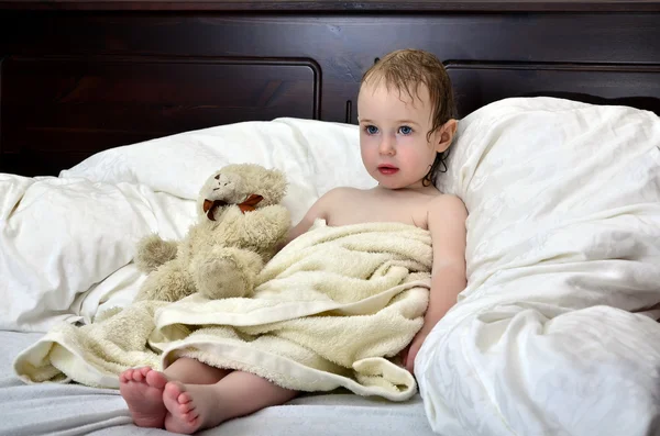 Bambina in un asciugamano dopo una doccia appoggiata su un letto — Foto Stock