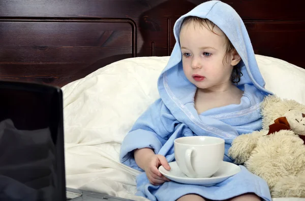 Little girl in a bathrobe relaxing on the bed after a shower with cup of te — Stock Photo, Image