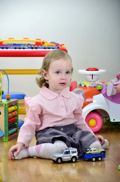 Menina em um quarto com brinquedos, brincando com carros — Fotografia de Stock