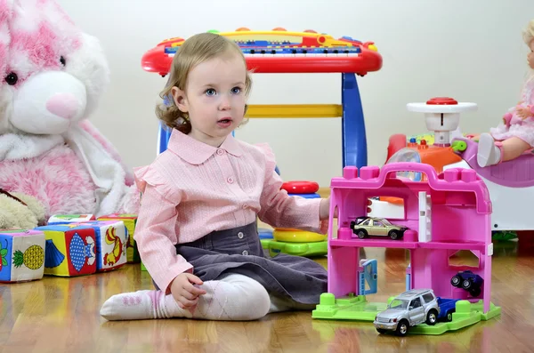 Liten flicka i ett rum med leksaker, leker med bilar — Stockfoto