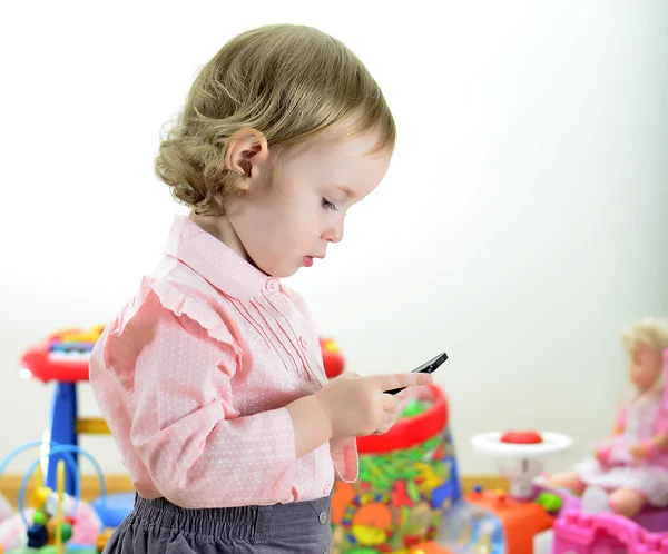 小女孩站在房间里拿着手机和玩具 — 图库照片