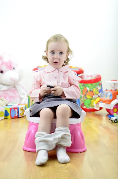 Μικρό κορίτσι που κάθεται στον ασήμαντο με τηλεχειριστήριο (ή κινητό τηλέφωνο), σε — Φωτογραφία Αρχείου