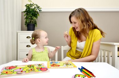 Little girl and mom playing in a children puzzle clipart