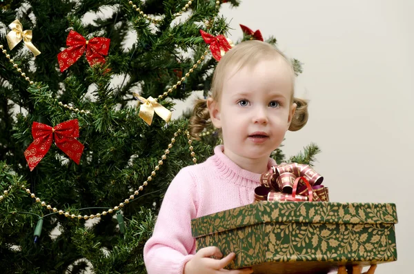 Liten flicka nära julgranen innehar en present — Stockfoto