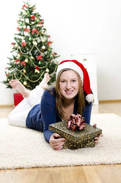 Navidad, la chica acostada en la alfombra con un regalo — Foto de Stock