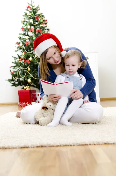 Chica y su mamá leyendo libro en Navidad —  Fotos de Stock