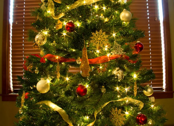 Ornamente, Lichter und Bänder auf leuchtend grünem Weihnachtsbaum Stockbild