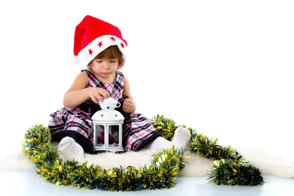 Little girl wearing a Santa hat and playing with baubles — Stockfoto