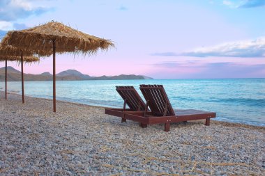 An attractive image of two chairs and umbrellas on the beach clipart