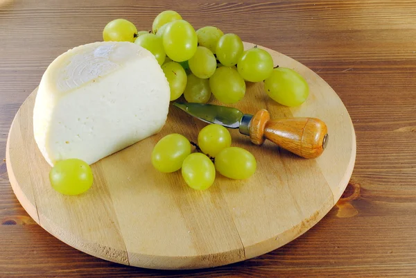 Italian cheese with grapes on wooden cutting board — Stock Photo, Image