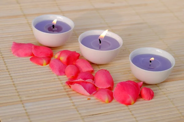 Tres velas moradas con pétalos de rosa en bambú — Foto de Stock