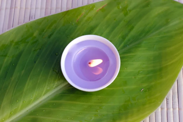 Purple candle on a green leaf over bamboo — Stock Photo, Image