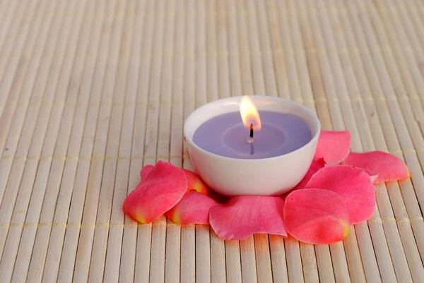 Candela viola con petali di rosa su bambù — Foto Stock