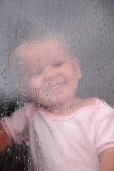 Bedårande barn tittar på regnet droppar vid fönstret — Stockfoto