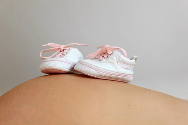Kleine Babyschuhe am Schwangerschaftsbauch — Stockfoto
