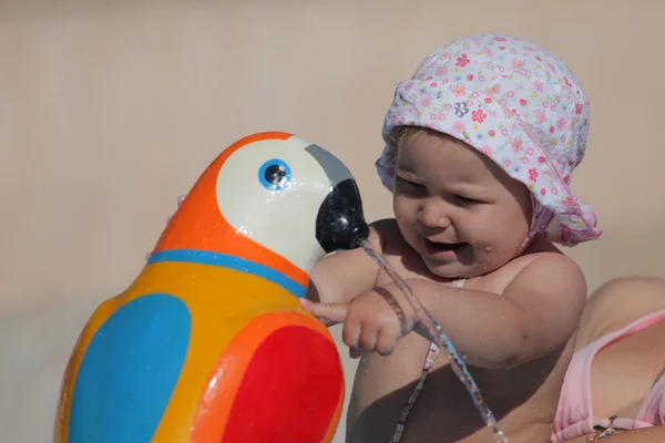 Cute toddler girl playing with a toy parrot at the pool — Stock Photo, Image