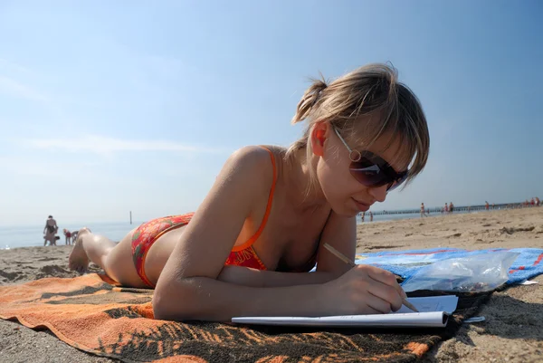 Girl lying on the beach and doing sudoku — Stock Photo, Image