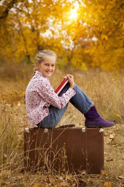La bambina sta leggendo un libro in legno autunnale — Foto Stock