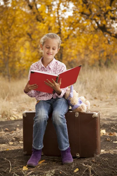 Little girl is reading a book in autumn wood — Stock Photo, Image