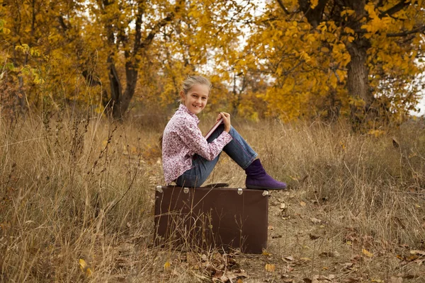 Klein meisje is het lezen van een boek in de herfst hout — Stockfoto