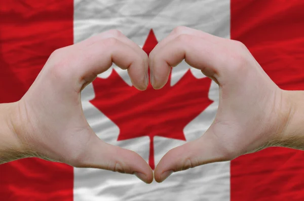 カナダの背景に隠れての旗上の手によって示した心と愛のジェスチャー — ストック写真