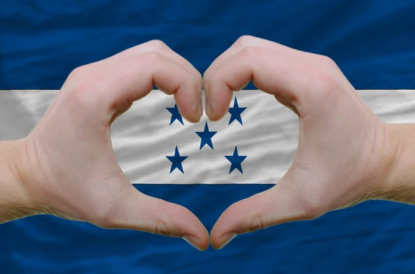 Srdce a lásku gestem ukázal rukou nad vlajkou Hondurasu bac — Stock fotografie