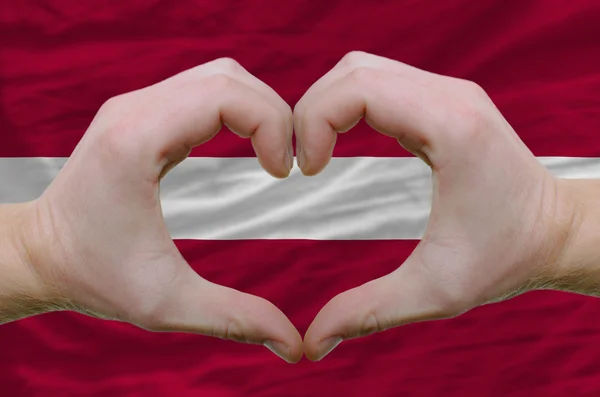 ラトビアの背景に隠れての旗上の手によって示した心と愛のジェスチャー — ストック写真