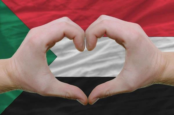 Srdce a lásku gestem ukázal rukou nad vlajkou Súdán pozadí — Stock fotografie