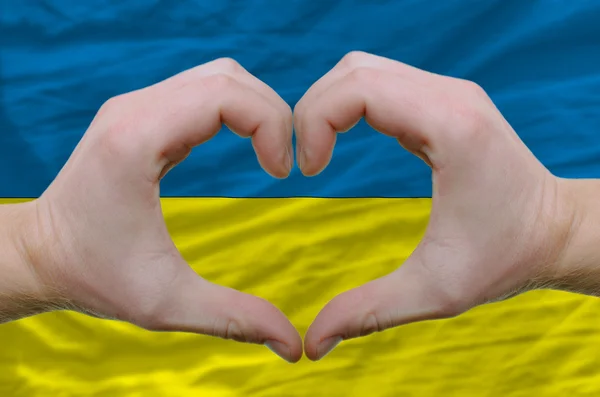 Καρδιά και αγάπη χειρονομία έδειξε από τα χέρια πάνω από τη σημαία της Ουκρανίας πίσω — Φωτογραφία Αρχείου