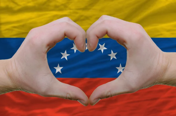 Srdce a lásku gestem ukázal rukou nad vlajka Venezuely ba — Stock fotografie