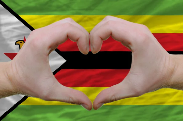 Srdce a lásku gestem ukázal rukou nad vlajka zimbabwe bac — Stock fotografie