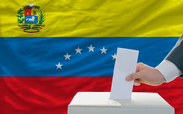 Мужчина голосует на выборах в Венесуэле перед флагом — стоковое фото