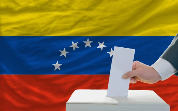 Мужчина голосует на выборах в Венесуэле перед флагом — стоковое фото