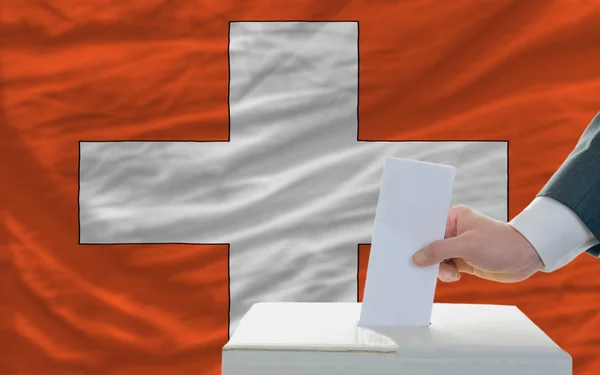 Мужчина голосует на выборах в Швейцарии перед флагом — стоковое фото