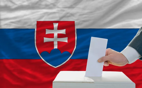 Мужчина голосует на выборах в Словакии перед флагом — стоковое фото