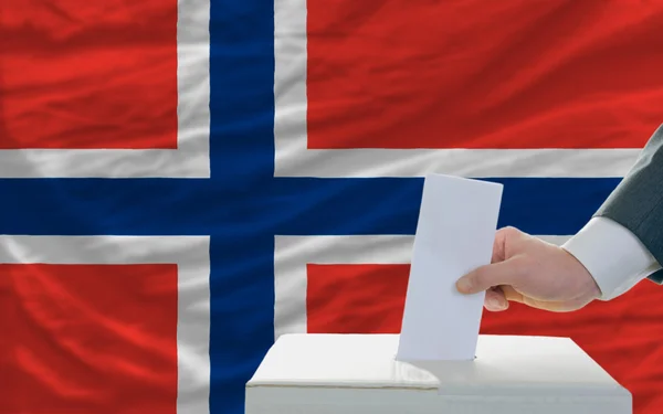 Мужчина голосует на выборах в Норвегии перед флагом — стоковое фото