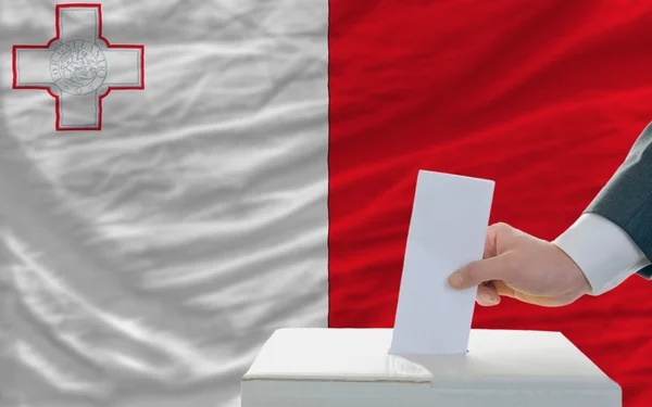 Мужчина голосует на выборах на Мальте перед флагом — стоковое фото