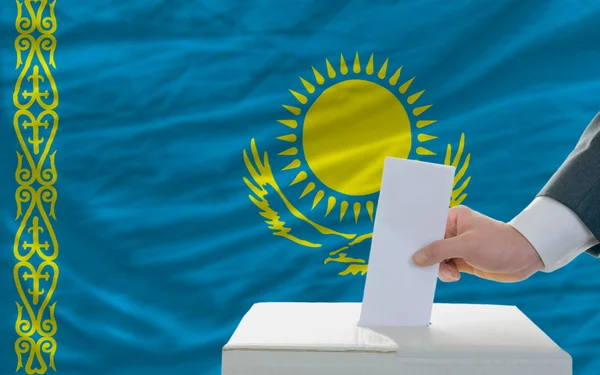 Мужчина голосует на выборах в Казахстане перед флагом — стоковое фото