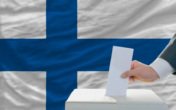 Мужчина голосует на выборах в Финляндии перед флагом — стоковое фото