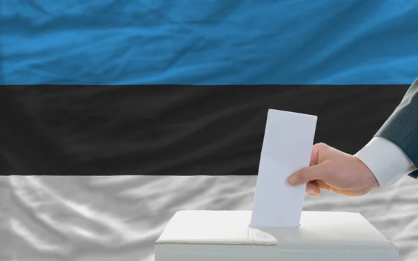 Uomo che vota sulle elezioni in estonia davanti alla bandiera — Foto Stock