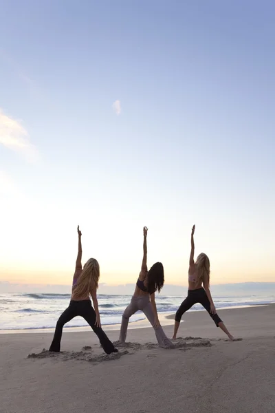 Tres mujeres practicando yoga en la playa al amanecer o al atardecer —  Fotos de Stock