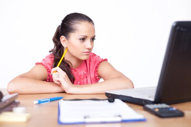 Beautiful young woman sitting at office desk and working on lapt clipart