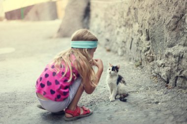 sarışın küçük kız street de kedi ile oynuyor.