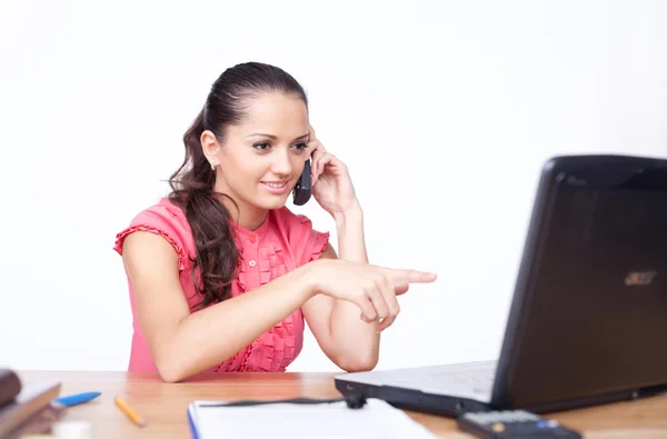 Beautiful young woman sitting at office desk and talking on cell — Stock Photo, Image