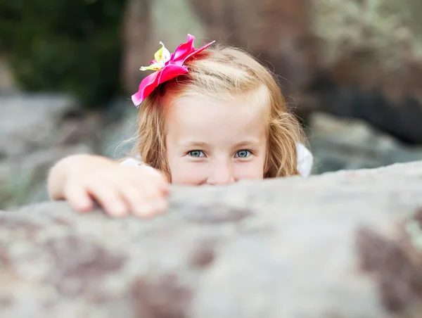 Beautiful blonde little girl girl hides behind a stone — Stock Photo, Image