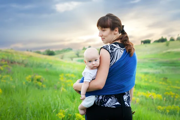 Mother and son in sling on green meadow at sunset in the summer — Stock Photo, Image