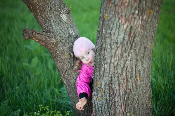Funny little girl hides behind tree in autumn — Stock Photo, Image