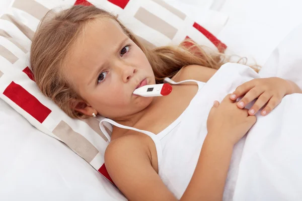 Больной ребенок в постели держит термометр между губами — стоковое фото
