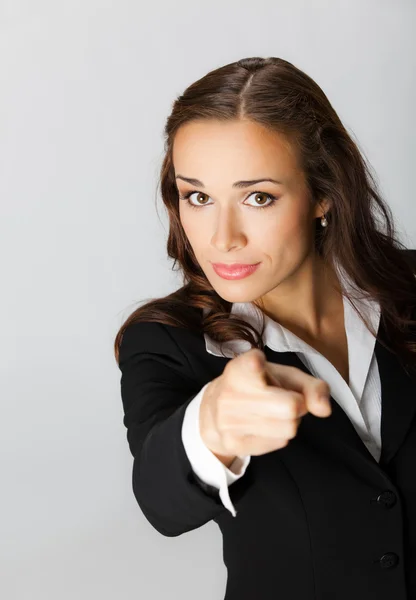 Serious business woman pointing finger at viewer, over grey — Stock Photo, Image