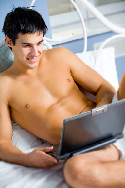 stock image Young happy smiling man working on laptop at bedroom